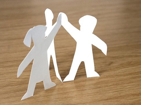 Team Drei ausgeschnittene Papierfiguren halten sich an den Händen auf einem Holztisch.