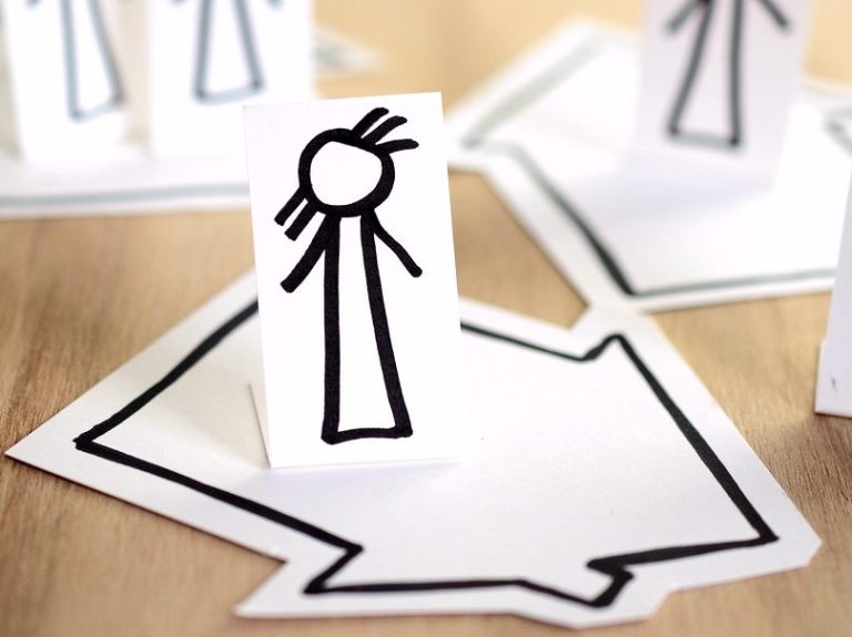 Einzelperson Zwei weiße Papierschnitte mit einfachen Strichfiguren und Pfeilen auf einem Tisch.